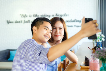 Homosexual lovers using a smart phone for take a selfie photo in a cafe.