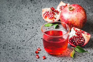 Pomegranate juice in glassand fresh ripe pomegranate fruit on dark concrete background. Selective focus,space for text.