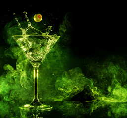martini cocktail splashing and green smoke in black background