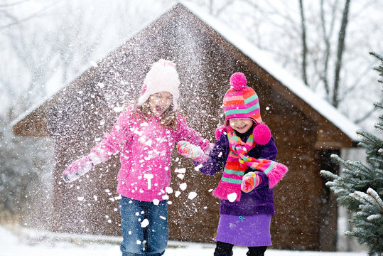 Happy sisters playing with snow during snowfall