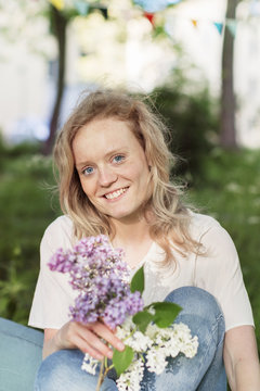 Outdoor portrait of smiling woman sitting with lilac flowers