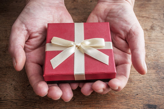 concept Saint Valentin  - détail mains d'homme tenant un paquet cadeau sur table en bois