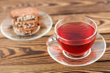 Full cup of red tasty raspberry tea and slice of roll pie on glass saucer on old wooden rustic table
