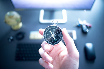 Ziele erreichen, Geschäftsidee. Kompass in der Hand, moderner Büroarbeitsplatz im Hintergrund