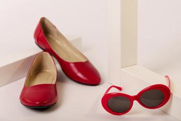 Female accessories of red color - shoes and sunglasses on a white background.