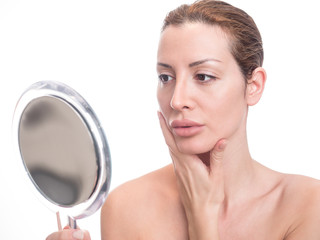 Displeased woman looking herself in a mirror. Isolated on white background.