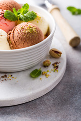 Assorted ice cream scoops of different colors and flavours in white bowl with pistachio nuts, chocolate and mint decoration. Summer food concept with copy space.