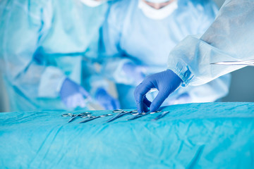 Medical team performing operation. Close up of scrub nurse taking medical instruments for operation with colleagues performing in background