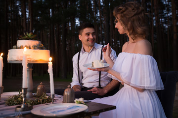 Newlyweds have fun having a wedding cake with candles in the evening in the nature