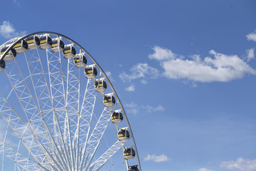 Giant Ferris wheel with numbered cabins in the park - Bright blue sky with sharp clouds behind it. - obrazy, fototapety, plakaty
