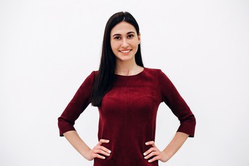 Young beautiful girl with black hair standing for white background holding her hands at waist