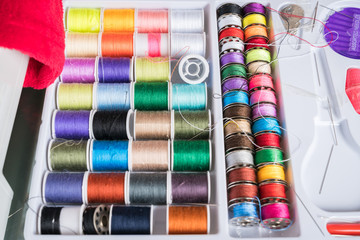 White plastic box inside Sewing kit with colored spools of threads and needles
