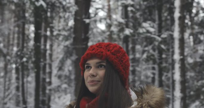 good looking girl brunnete woman enjoying winter nature, standing in the forest or park, smiling, wearing red cap and scarf