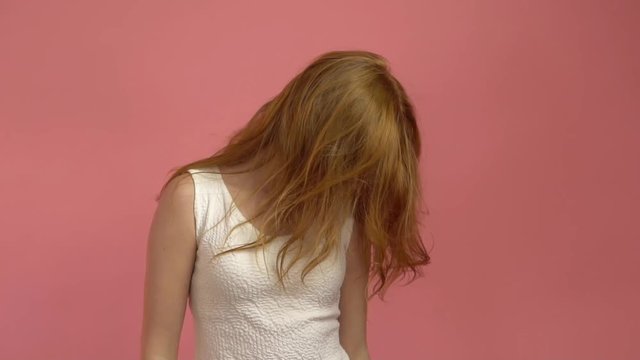 Beautiful teenage girl with red blowing hair and blue eyes on pink background