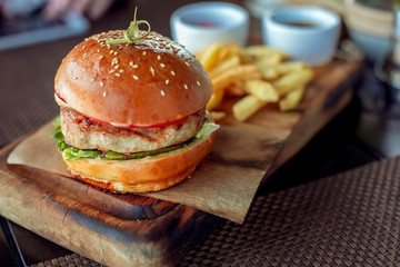 Appetizing burger with French fries and sauce on a wooden board