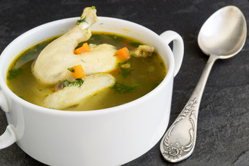 Chicken soup with vegetables on a black background.