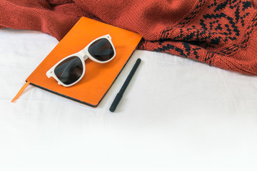 Sunglasses white frame and orange notebook lying on the knitted fabric. White background. Copy space, mock up