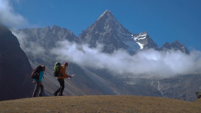 Hikers with backpacks travel in the Himalayan mountains. The map helps you to choose the right path. 4K