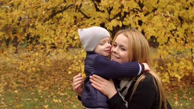 Funny mother and son kissing on the background of a big autumn tree in the Park.
