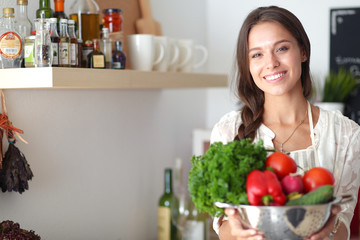 Obraz na płótnie Canvas Smiling young woman holding vegetables standing in kitchen. Smiling young woman