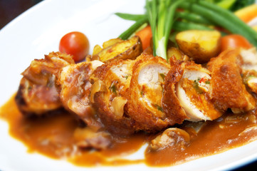 Cooked chicken with sauce and vegetables on a white dinner plate. 