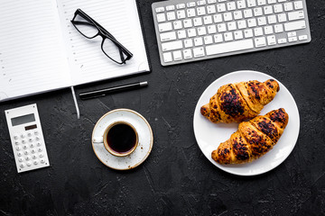 Morning of businessman. Coffee and croissants for breakfast near keyboard and notebook. Black background top view