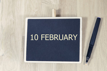 sentence FEB 10 written with chalkboard on a wooden table with pen.