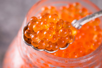 Red caviar in glass jar with silver spoon close up. Sea food. Healthy eating.