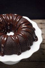 Close Up of Dark Chocolate Ganache Covered Bundt Cake on White Cake Stand