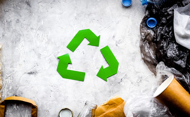 Eco-friendly life. Green paper recycling sign among waste paper, plastic, polyethylene on grey...