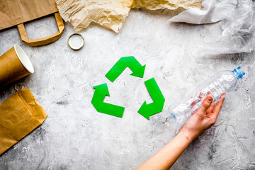 Eco-friendly life. Green paper recycling sign among waste paper, plastic, polyethylene on grey...