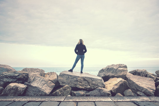 woman standing on the rock at the seaside, blonde young lady looking far away