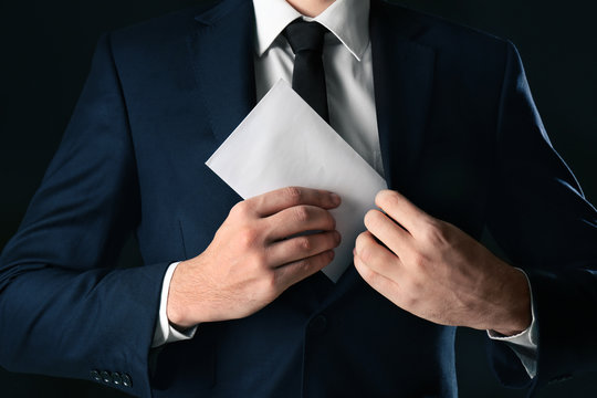 Businessman putting envelope with bribe in pocket on black background