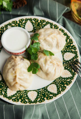 Asian Uzbek manti dish with sour cream on a green napkin with chickpeas and spices