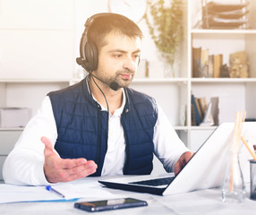 Young male employee with headset and laptop at table