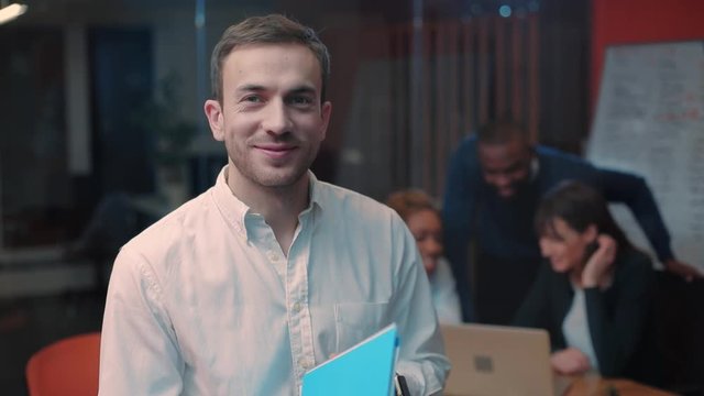 Likable smart young man in business clothes reading documents, slamming blue folder. Guy looking carefully at camera