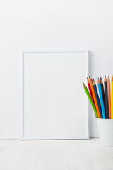 Fototapeta premium White Frame Mock Up with Space for Artwork Lettering Calligraphy Text Inspirational Quote. Multicolored Pencils in Bucket. Creativity Diversity Business Product Branding Promotion. Copy Space