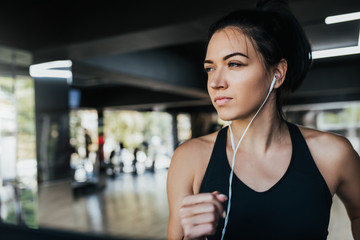 Fototapeta na wymiar Horizontal shot of young Caucasian woman runner listening music on earphones while running in the gym, wearing black sportswear. People, sport and fitness concept.