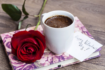 coffee cup with red rose and happy valentines message card on a book