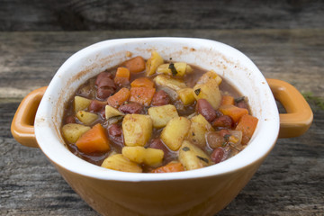 Appetizing beautiful soup with potatoes, onions, carrots and beans. On an old wooden background and close-up.