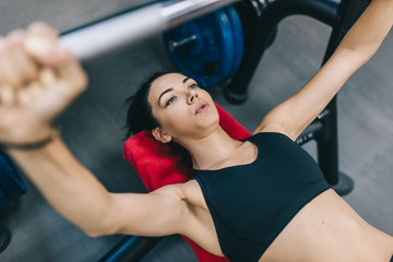 Above view of sporty attractive muscular young woman workout in a gym, lying on a bench, lifting weights with barbell. People, sport, fitness concpet.