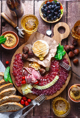 Mix of different snacks and appetizers: sausage, bread, olives, cheese, chestnuts, peas and beer on wooden board. Top view.