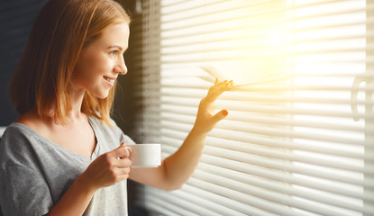 Happy young woman meets   morning with  cup of coffee  at   window