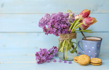 cup of coffee with biscuits and bouquet of lilac on white wooden background