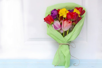 bouquet of colorful tulips wrapped in green paper on  a wooden  background 