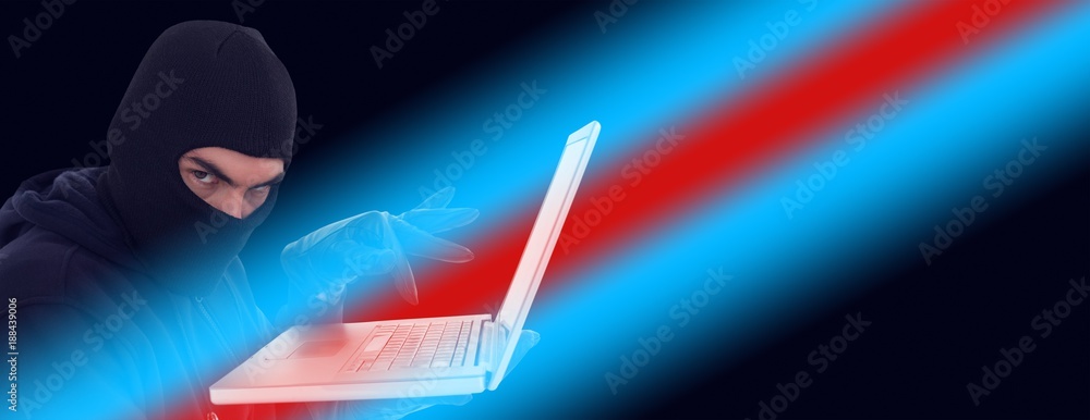 Poster hacker in balaclava standing and typing on laptop