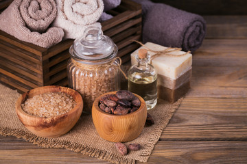 Fototapeta na wymiar Natural cosmetic oil, sea salt and natural handmade soap with cocoa beans on rustic wooden background