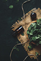Essential oregano oil in a glass bottles and a bunch of fresh herbs, black background, top view