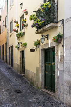 Narrow street and the facade of a building with flowers in the traditional neighborhood of Alfama in Lisbon, Portugal; Concept for visit Lisbon