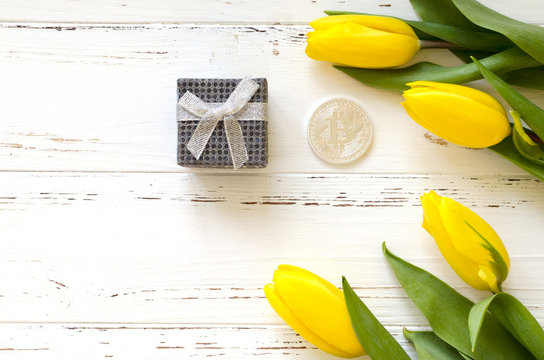 silver bitcoin, gift box, yellow tulips on wooden background - Powered by Adobe
